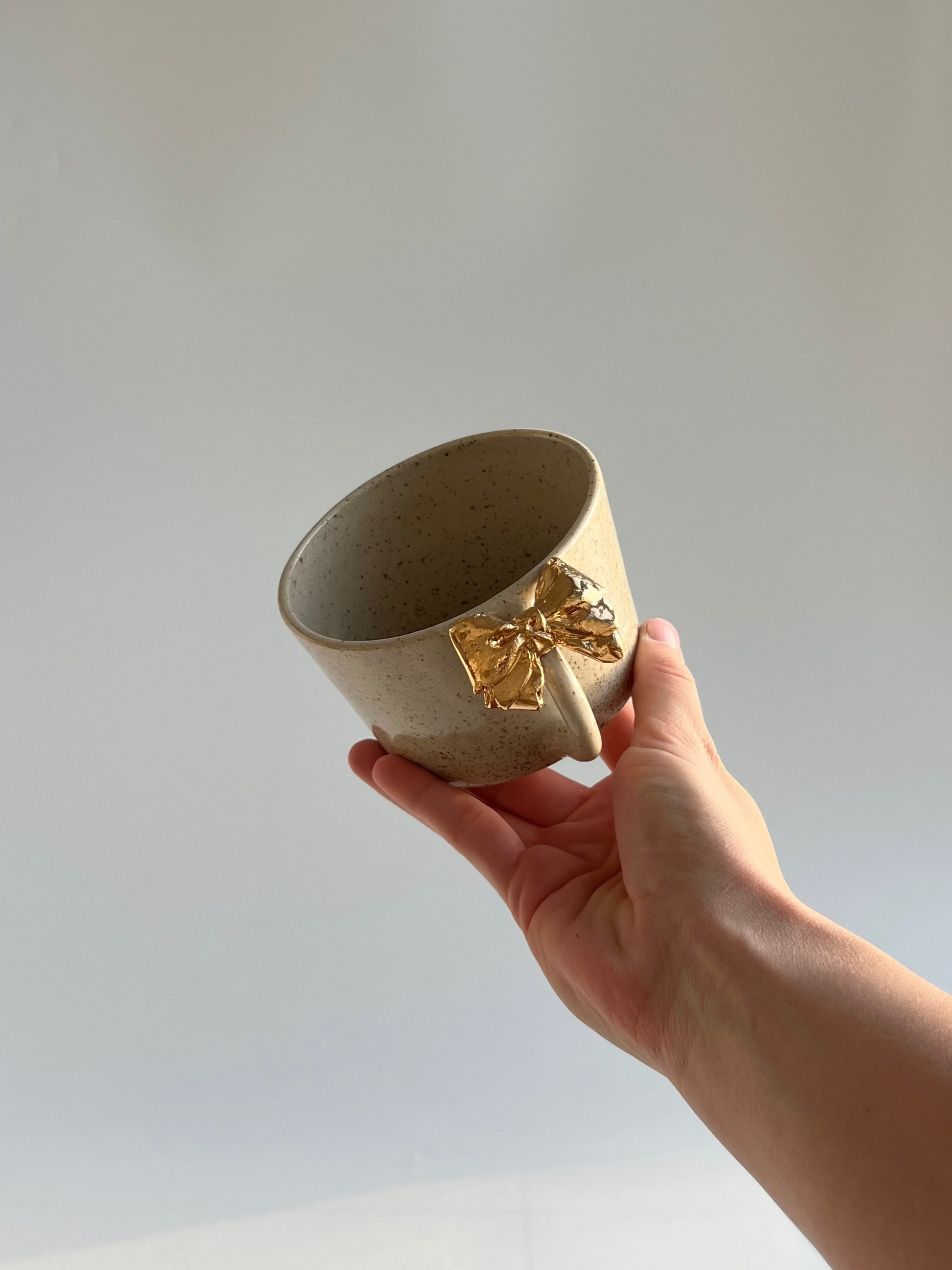 Hand holding a ceramic cup with gold accents against a plain background